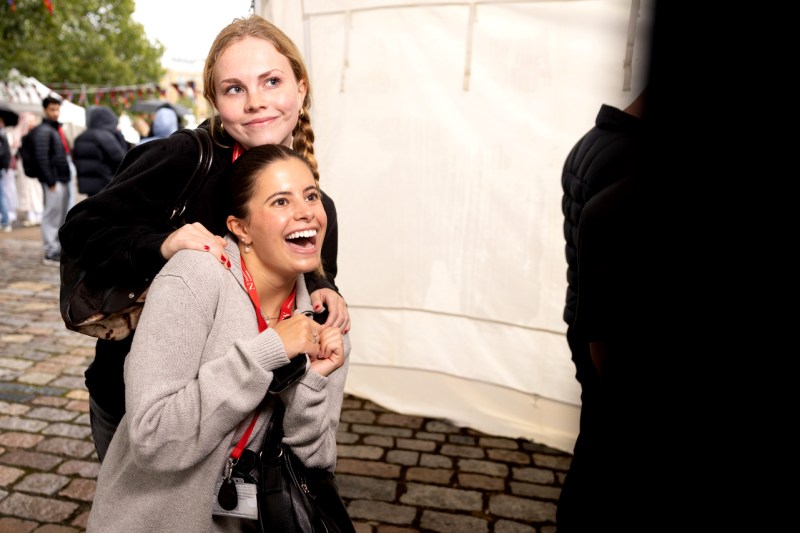 Two light-skinned female students pose of a photo in front of a white tent.