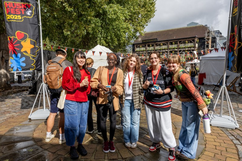 A group of students shown smiling together for a photo in front of the Husky Fest sign.