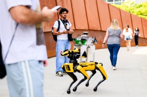 A Boston Dynamics Spot robot, equipped with sensors, walks alongside students near the ISEC and EXP buildings on Northeastern’s Boston campus.
