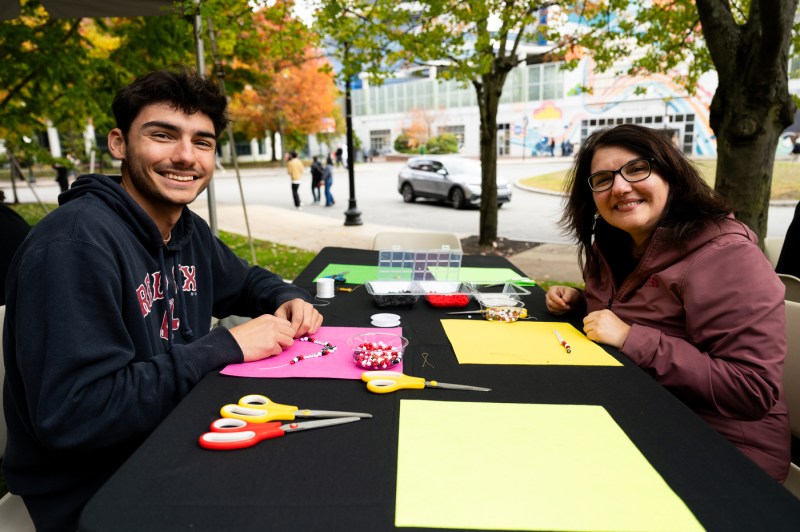 Tyler Pilch, an environmental engineering student at Northeastern, and his mother Claudia Pilch make friendship bracelets together during the Friends and Family Weekend Fall Festival on Centennial Common.